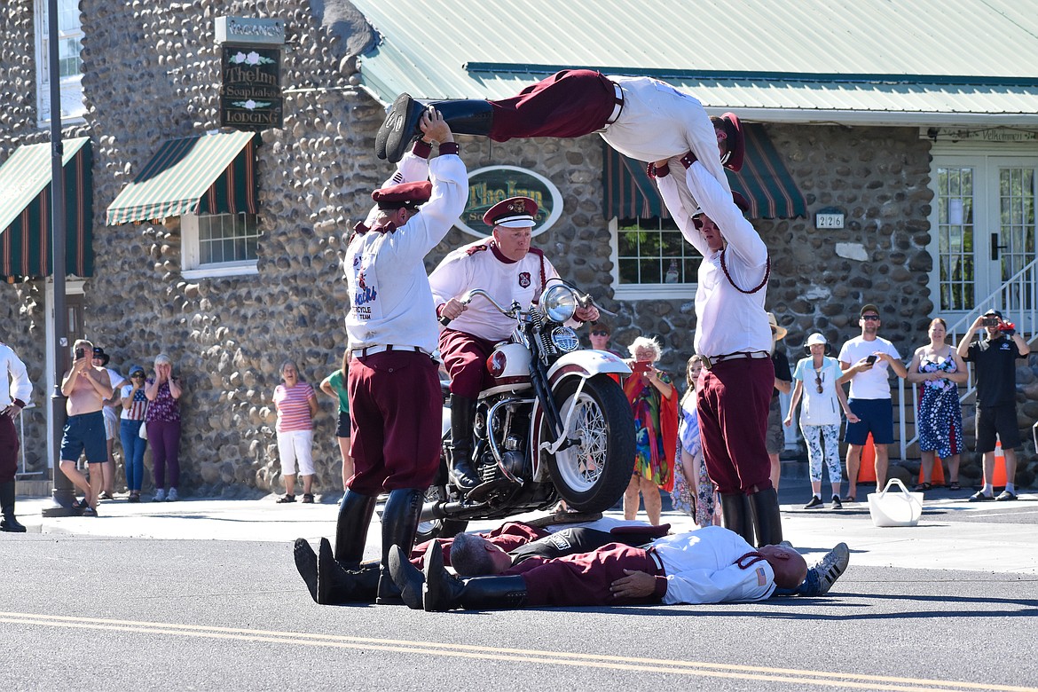 Three people lay underneath a wood ramp while two Cossacks hold a third up in the air for the motorcycle rider to go through.