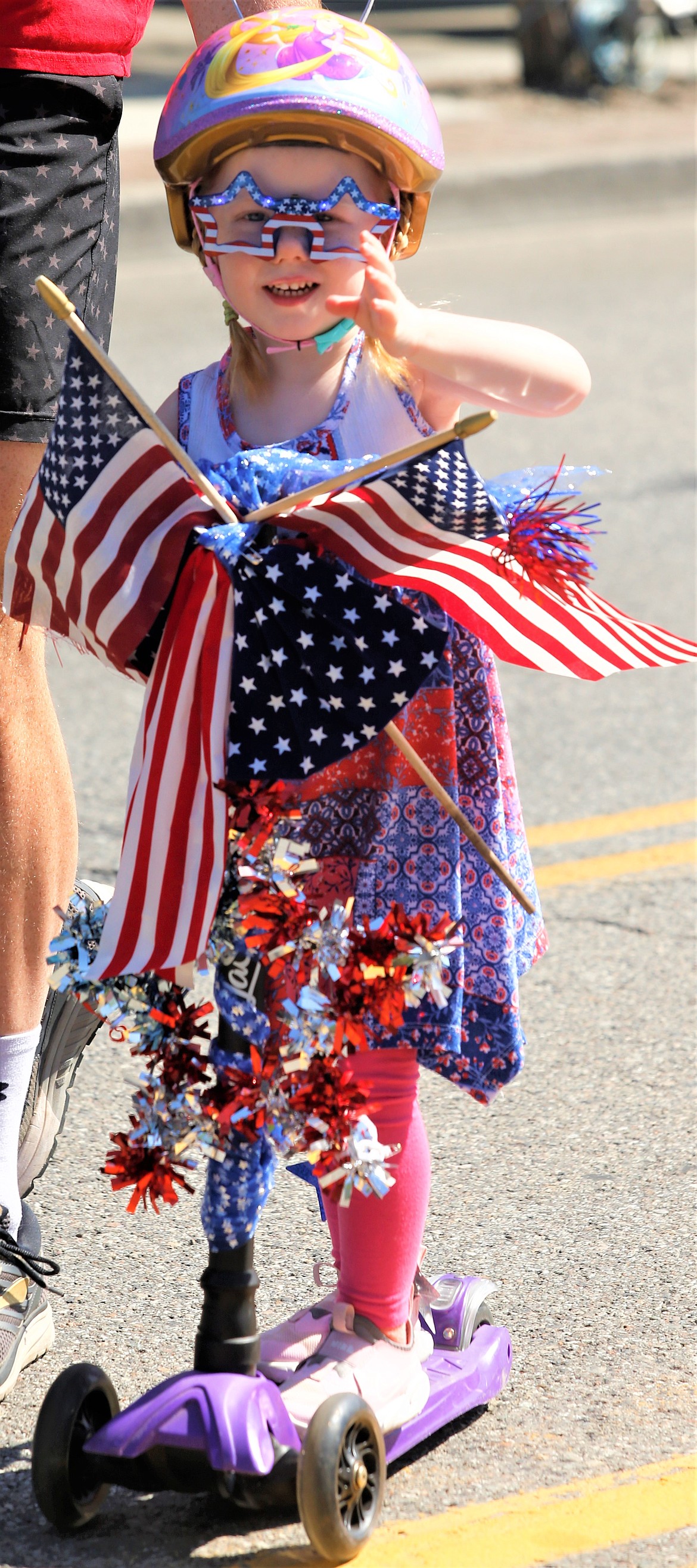 Rory O'Brien waves as she rides her scooter through the annual Kiddies Parade on Sherman Avenue on Monday.