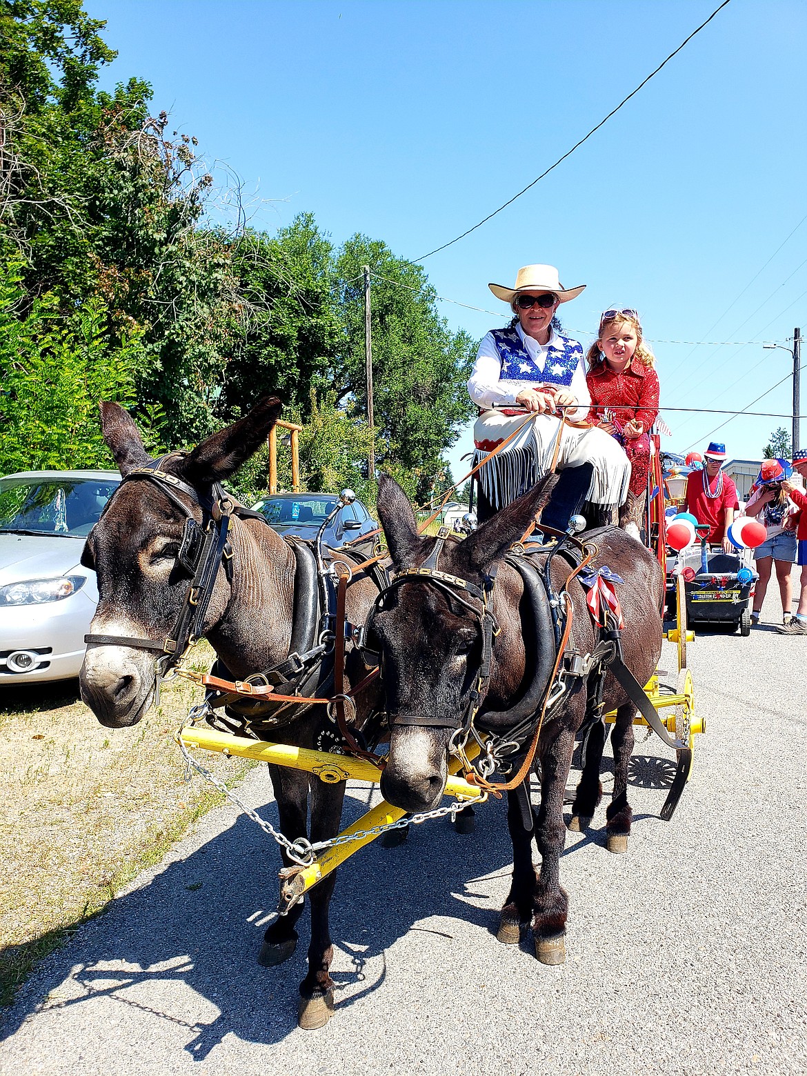 North Idaho Saddle Mule Club mules Calvin and Hobbes pull a cart as Valerie Larson steers and Hadley Reed rides along to wave at spectators in the Spirit Lake Old Fashioned Fourth of July Parade.