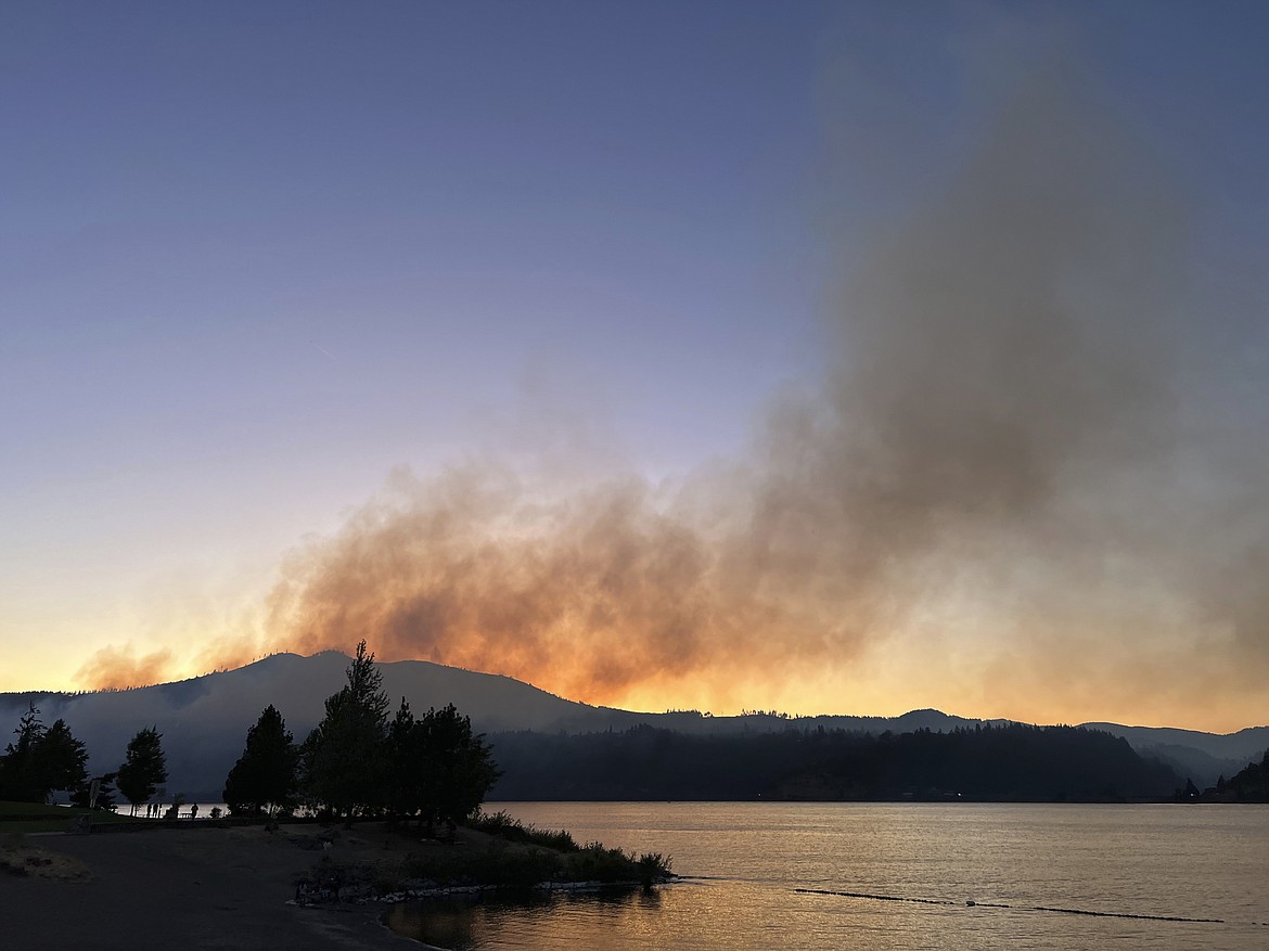 Smoke from a wildfire in the Columbia River Gorge in Washington State rises in the background in this view Hood River, Ore, Sunday, July 2, 2023. Authorities have more than doubled the number of people battling the wildfire that has burned some homes and forced the evacuation of hundreds of others in southwestern Washington near the Columbia River Gorge. (Joel Odom/The Oregonian via AP)