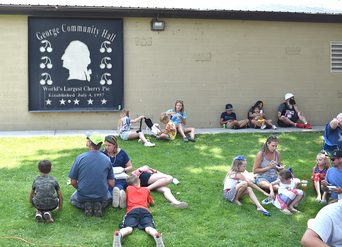 Revelers enjoy shade and cherry pie on the grass beside the George Community Hall during the Independence Day celebration Tuesday. The sign on the side of the hall is made from the original pan that was formerly used to bake the pie, according to Georgette Sandra Marcuson.