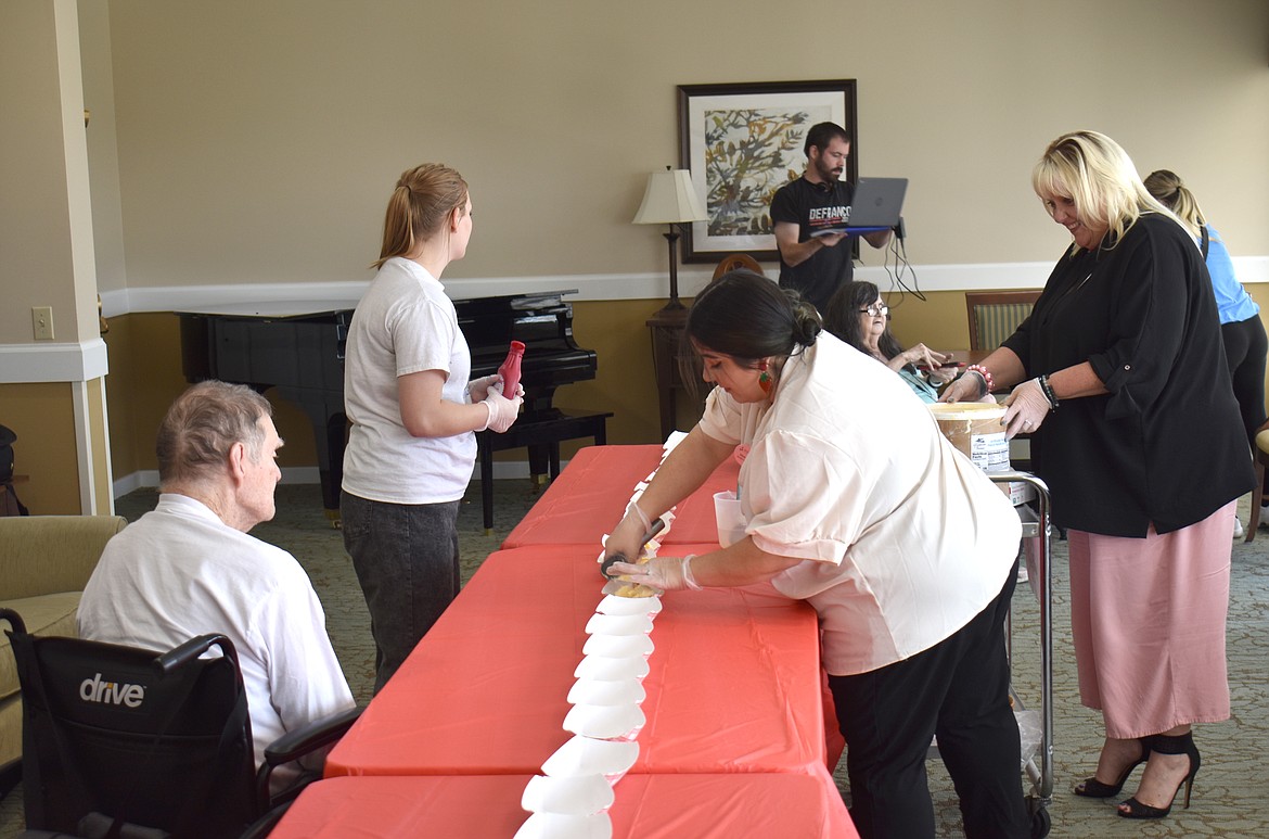 Brookdale Hearthstone Activity Director Aleecia Robledo scoops ice cream into bowls while resident Dave Roberts watches and Kendall Vance, left, and Kar Vanerstrom stand ready with more supplies for the 20-foot strawberry sundae they created to mark National Strawberry Sundae Day.