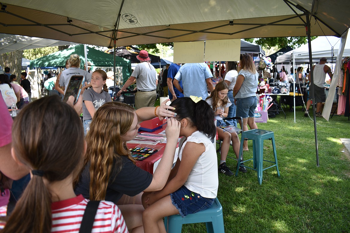 Haley Piercy paints flowers on Amy Cedillo, 6, at Summerfest Saturday. Piercy is a 2023 graduate of Royal High School.