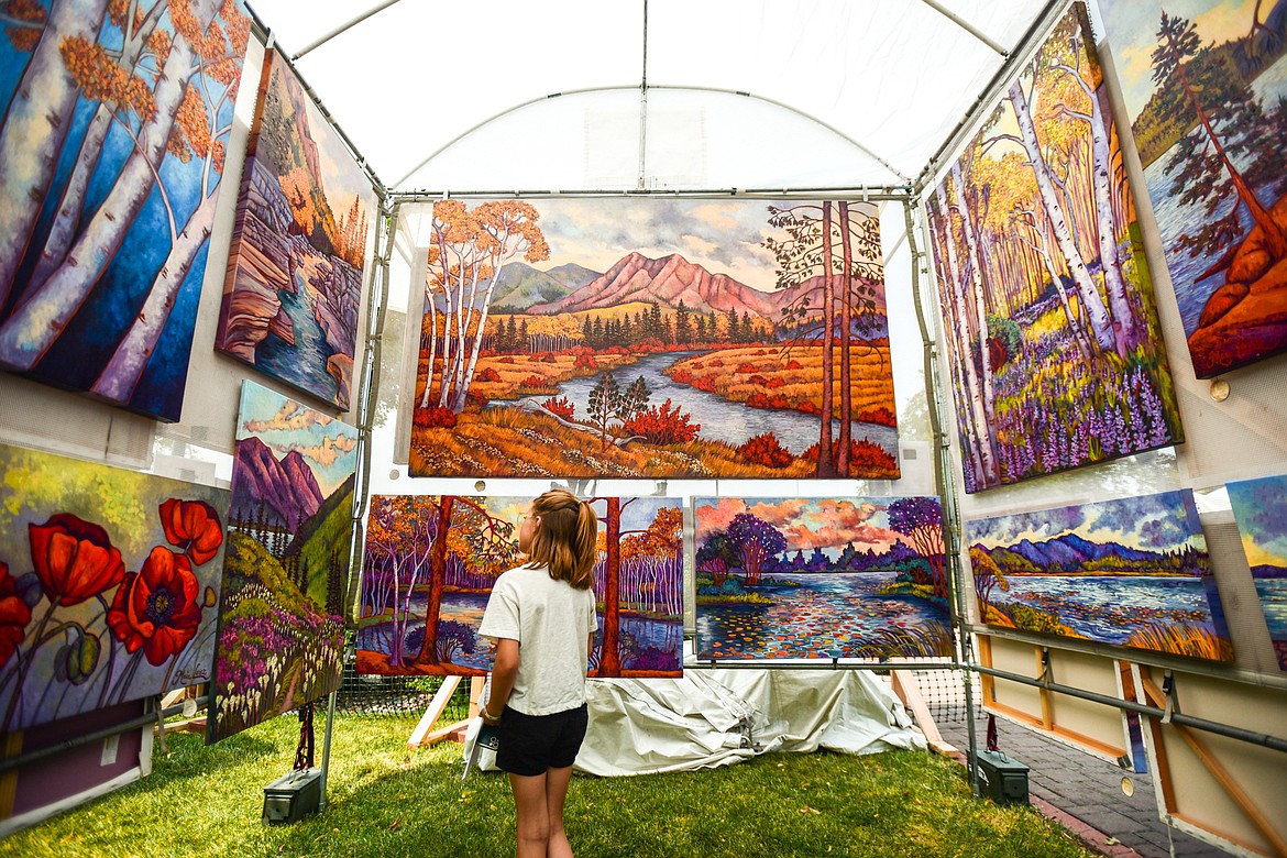 A young girl looks over the custom giclee prints of fine artist Maia Leisz at her stand at the Hockaday Museum's Arts in the Park festival at Depot Park on Friday, July 14. The festival also features food and specialty booths, live music and entertainment from over 40 performers, a premium wine and beer garden and a new community corner with booths and activities presented by local institutions. (Casey Kreider/Daily Inter Lake)