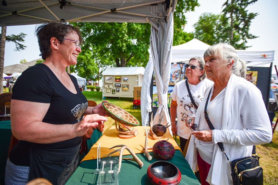 Artist Michelle Ellen, left, of Ever Altering Wood Studio in Missoula, shows visitors one of her hand-crafted wooden basket platters at the Hockaday Museum's Arts in the Park festival at Depot Park on Friday, July 14. The festival also features food and specialty booths, live music and entertainment from over 40 performers, a premium wine and beer garden and a new community corner with booths and activities presented by local institutions. (Casey Kreider/Daily Inter Lake)