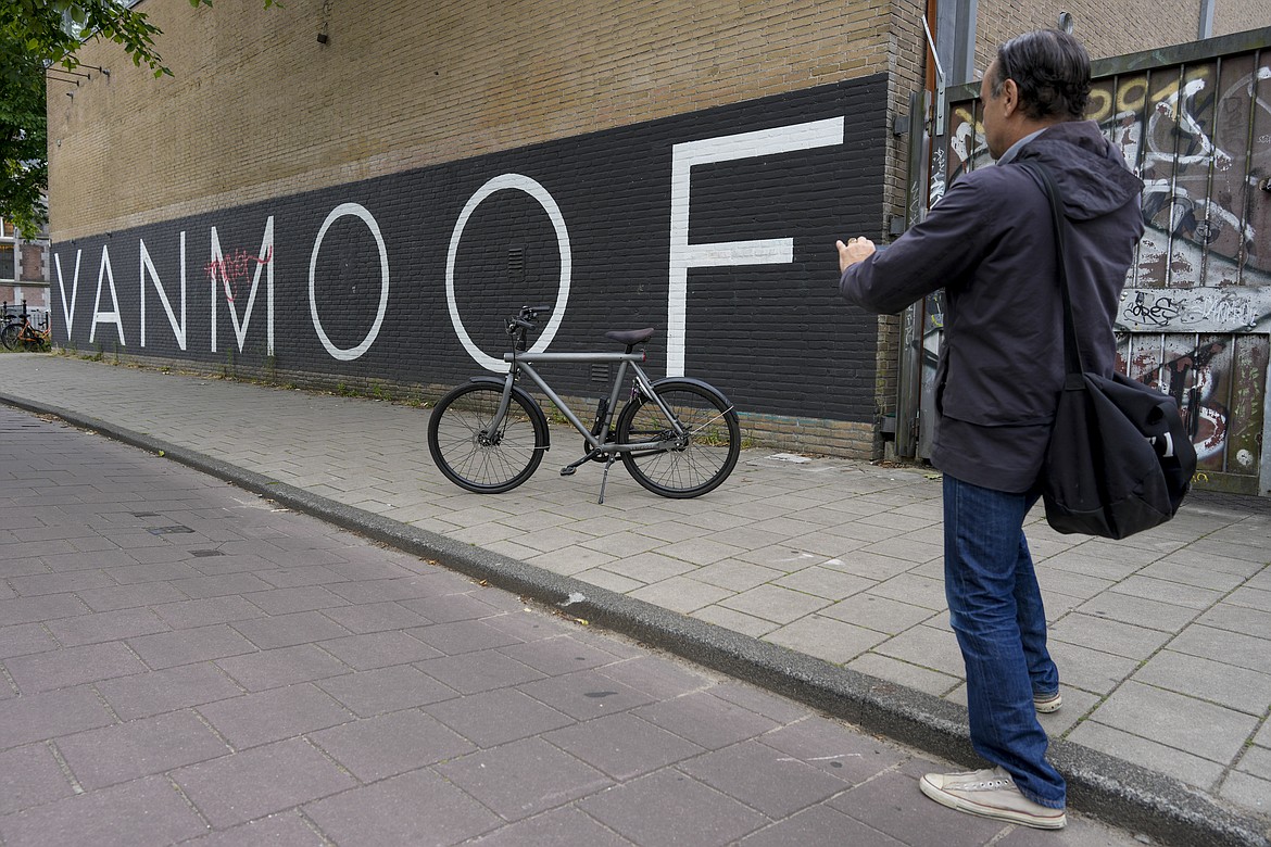 A man parked his VanMoof bicycle outside the VanMoof head office to take a picture in Amsterdam, Netherlands, Tuesday, July 18, 2023. Dutch electric bicycle maker VanMoof has been declared bankrupt, slamming the brakes on a company that won design awards for its pared-back electric bikes but struggled to meet soaring demand and fix glitches. (AP Photo/Peter Dejong)