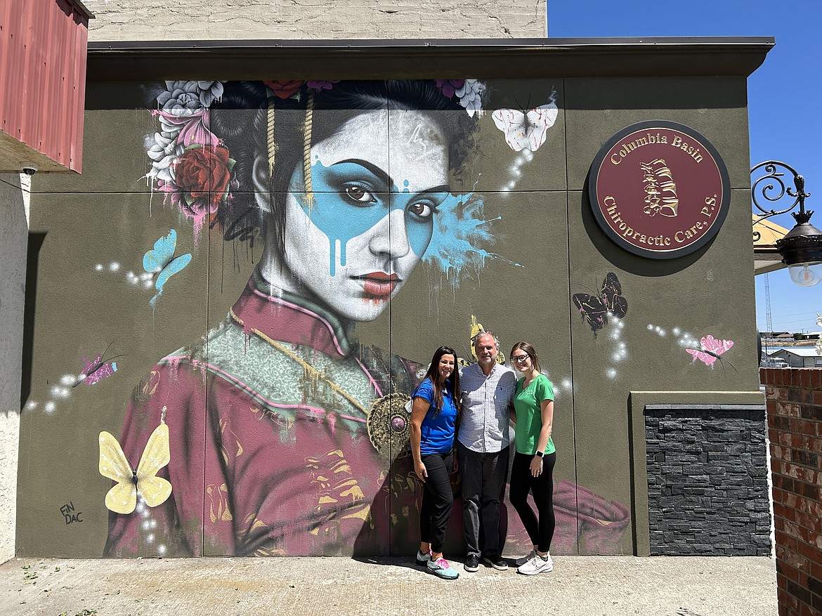 Nicole Lamens, left, Dr. Brent Bedford, middle, and Haley Dockins, right, stand on the side of Columbia Basin Chiropractic in front of the mural painted by famous street artist Fin DAC.