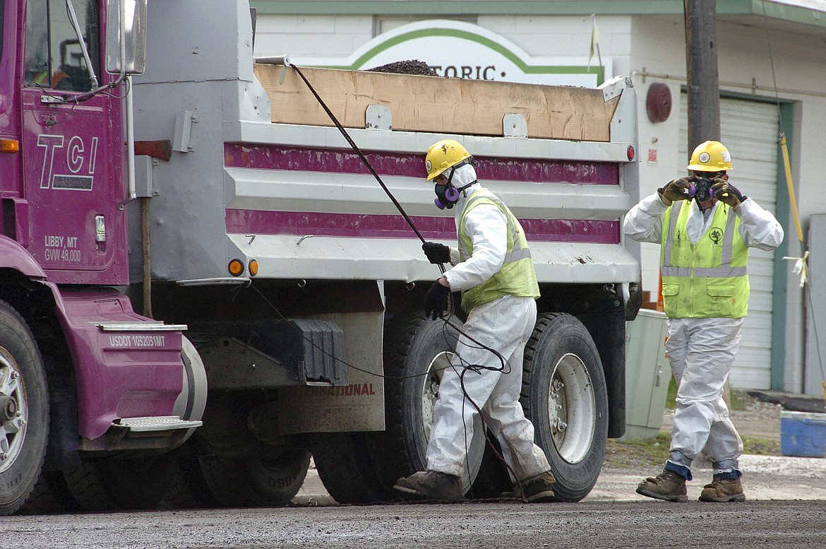 Unidentified road workers wear protective gear against possible asbestos contamination as they load material from a road resurfacing project in downtown Libby, Mont., April 28, 2011. A health clinic in the Montana town that's plagued by deadly asbestos contamination is liable for almost $6 million in penalties and damages after it submitted hundreds of false claims for government benefits. (AP Photo/Matthew Brown, File)