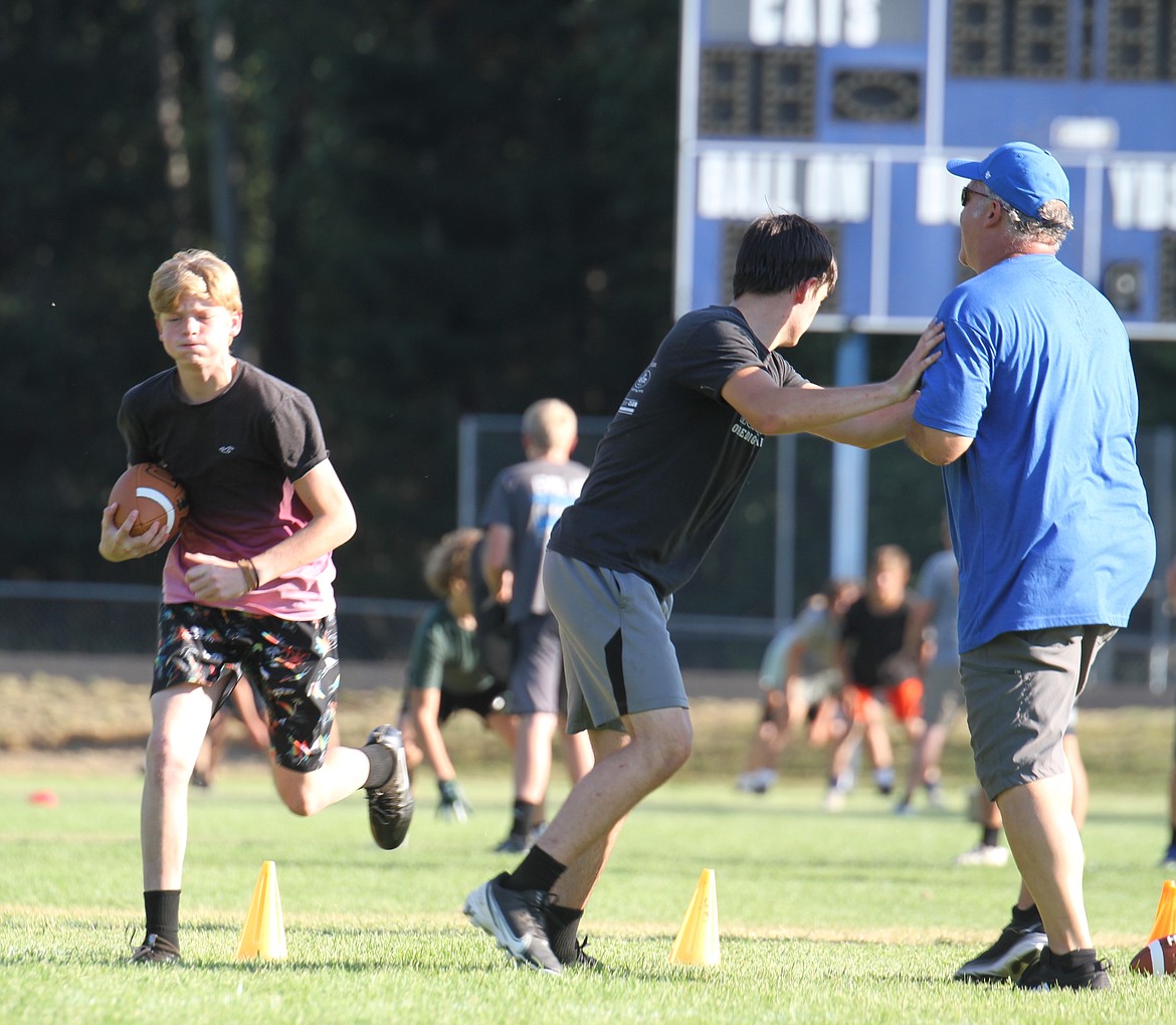 Athletes participate in a running and blocking drill with the help of a coach.
