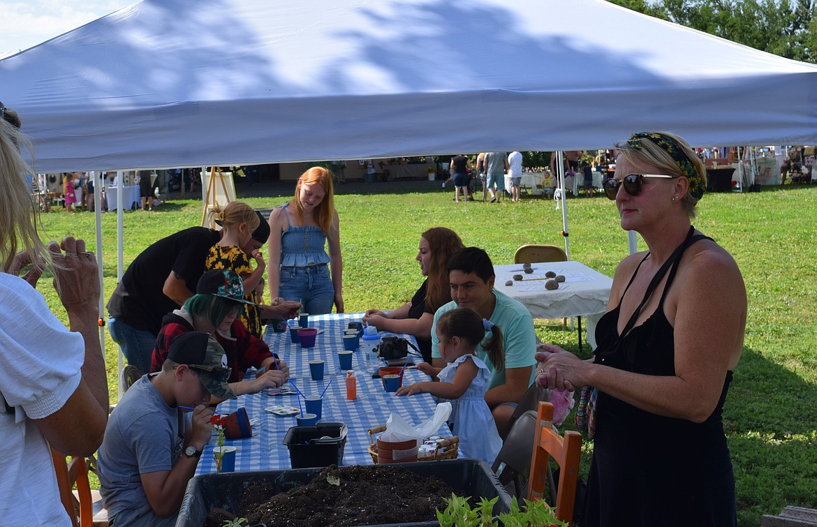 Katie Jo Buchanan, right, leads event attendees at the Paint-a-Pot station at Cloudview Farm’s Summer Sunflower Fest. Children and adults painted their own pots and chose flowers to plant in them.