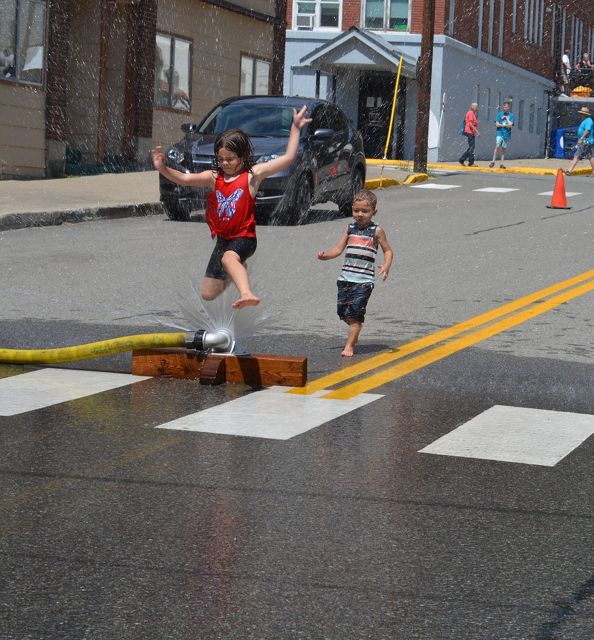 McKenna Barnes, 7, jumps through a sprinkler during the Mullan Fireman's Fun Festival.