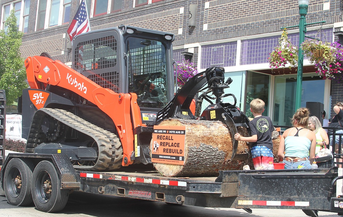 A float consisting of a Kubota track loader holding a log makes its way downtown on Saturday. On the log is a "Recall. Replace. Rebuild." sign that refers to the controversy surrounding the West Bonner County School District.