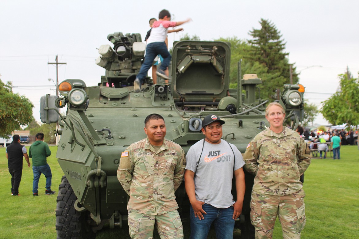 Javier Rodriguez, left, and Kay Monroe, right of the Washington National Guard pose for picture with a native of the Rodriguez family’s Mexican hometown while children play on the Stryker personnel carrier they brought to National Night Out.