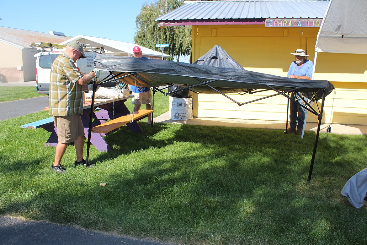 Ephrata Lions members, from left, Roger Adams, Bill Sangster and Rock Witte erect an awning outside the Lions food booth at the Grant County Fairgrounds. The fair starts today, and the forecast is for 100-degree weather the first three days.