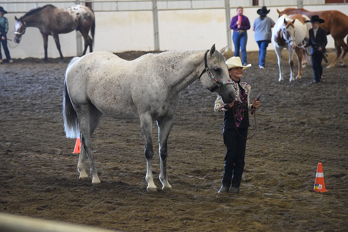 A young lady holds her horse as she prepares to begin her run through the course for judging. Her purple, black and white outfit was one of many traditional Western outfits competitors wore for the horsemanship competition.