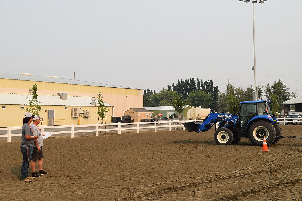 Event organizer Austin Kern, left, and his father watch a competitor carefully during Saturday’s FFA tractor driving contest at the Grant County Fair.