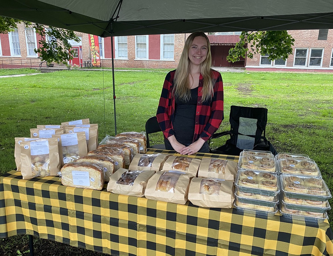 Tessa Clark, stands with a table full of her freshly baked breads, buns, and rolls, during the Superior Farmer's Market last Saturday. Now as the market days wind down, Clark will continue baking her delectable treats but through an order and delivery/pickup service. (Photo courtesy/Tessa Clark)