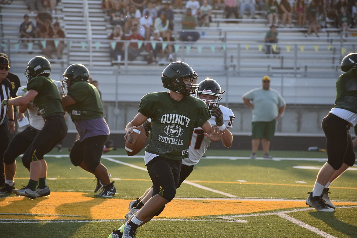 A Quincy quarterback runs to his right at the Quincy jamboree, evading Ephrata defenders.