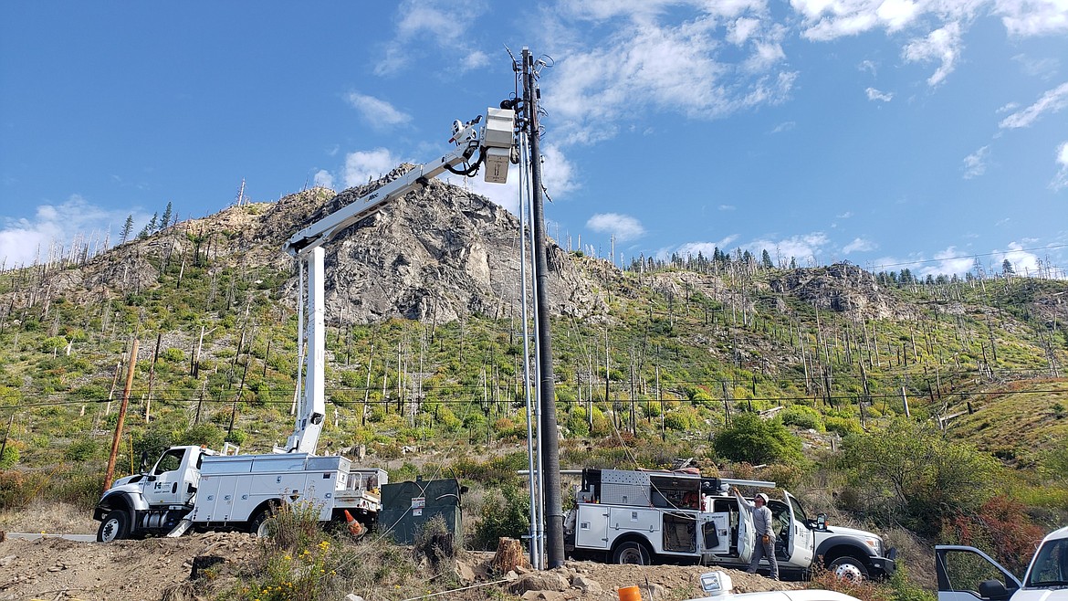 Kootenai Electric Cooperative crews work on a power line, with the skeletons of trees in the background. Dead or weakened trees can be a fire hazard when they’re too close to electrical lines.