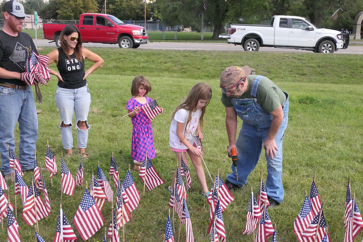 Cora Coonon (blue/pink dress) and her sister Ulah help local Vet Ed Foste plant a row of flags at the exhibit to raise attention to veteran suicides.  The exhibit is in the green stretch of park along Highway 200 in Plains. (Chuck Bandel/VP-MI)