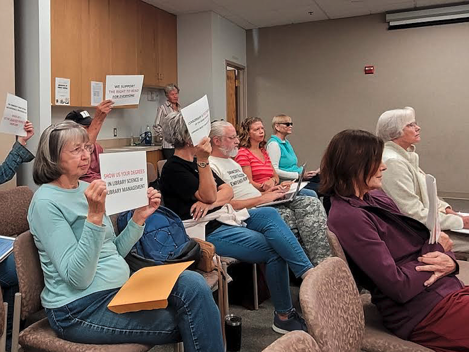 Carolyn Mattoon, left, and other library supporters hold up signs during a special Friday morning meeting of the Community Library Network's board of trustees at the Post Falls Library.