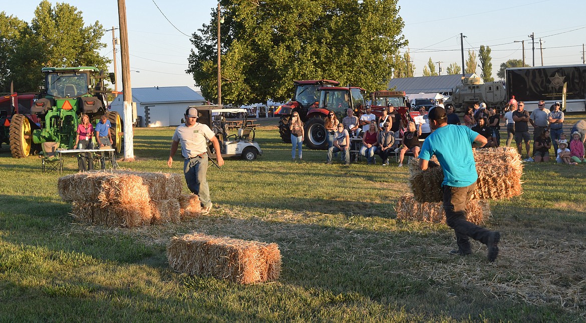 One hay bucking team member carries a bale of hay to the other team member, the stacker. After the bales are stacked, the team members switch roles and re-stack all the hay.