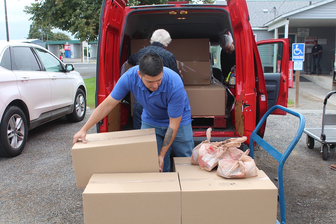 Othello Food Bank Director Jose Garza, front, unloads food destined for the Bites 2 Go program. Bites 2 Go provides food to children during weekends.