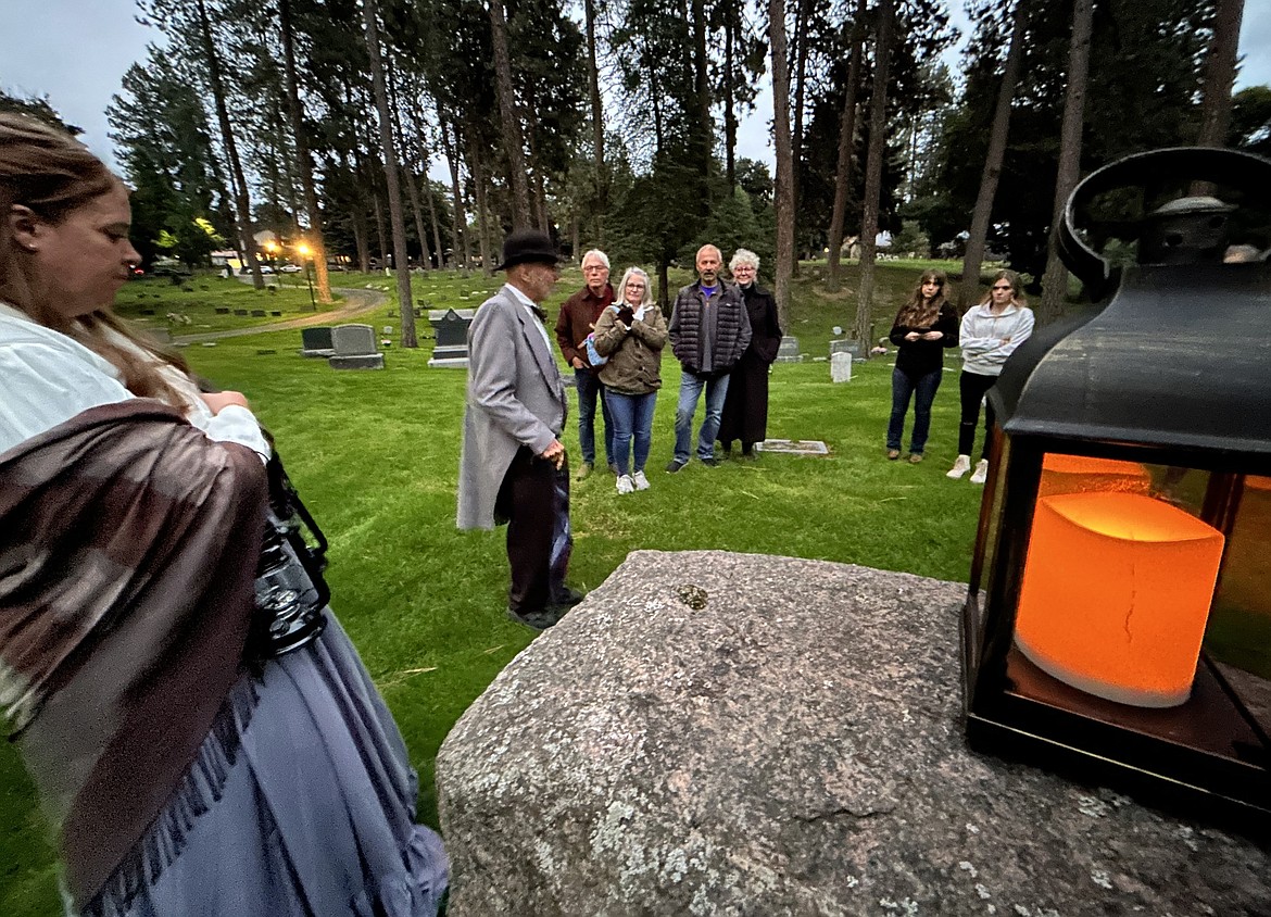Dave Eubanks, wearing a derby hat, talks about Coeur d'Alene's history during a tour of Forest Cemetery with about 20 people Friday evening.