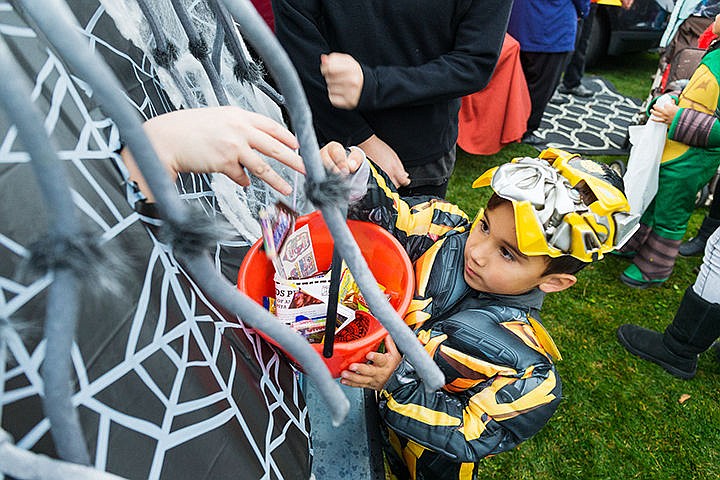 Braxson Seath, 5, hoists his bucket up for a mysterious hand that drops candy from the back of a vehicle at a park near the intersection of Sixth Street and Sherman Avenue Friday as part of the Coeur d'Alene Downtown Association's new "Trunk or Treat" event.
