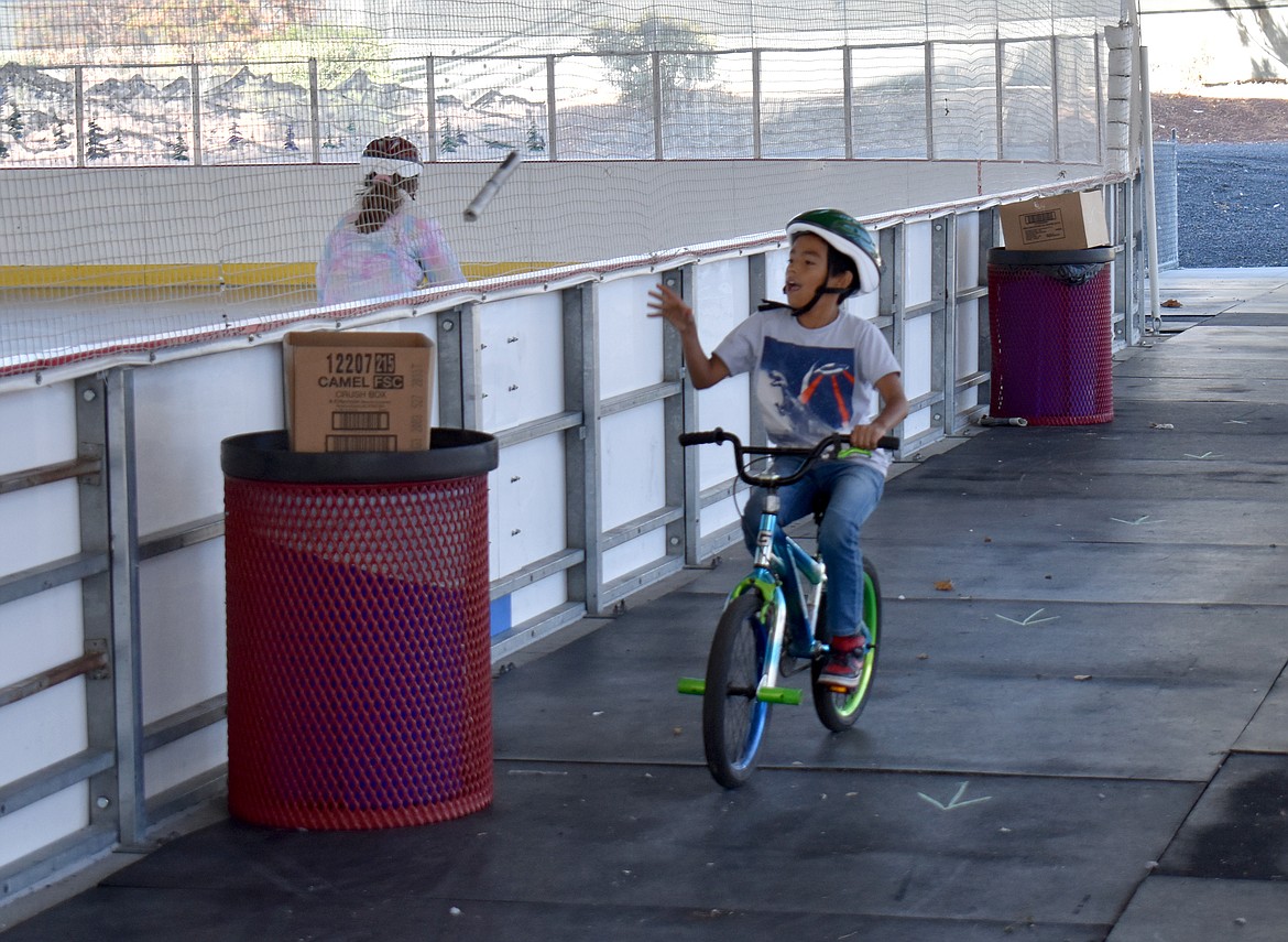 A young rider takes aim and tosses a newspaper into a box at the annual bike rodeo at the Larson Recreation Center Saturday.