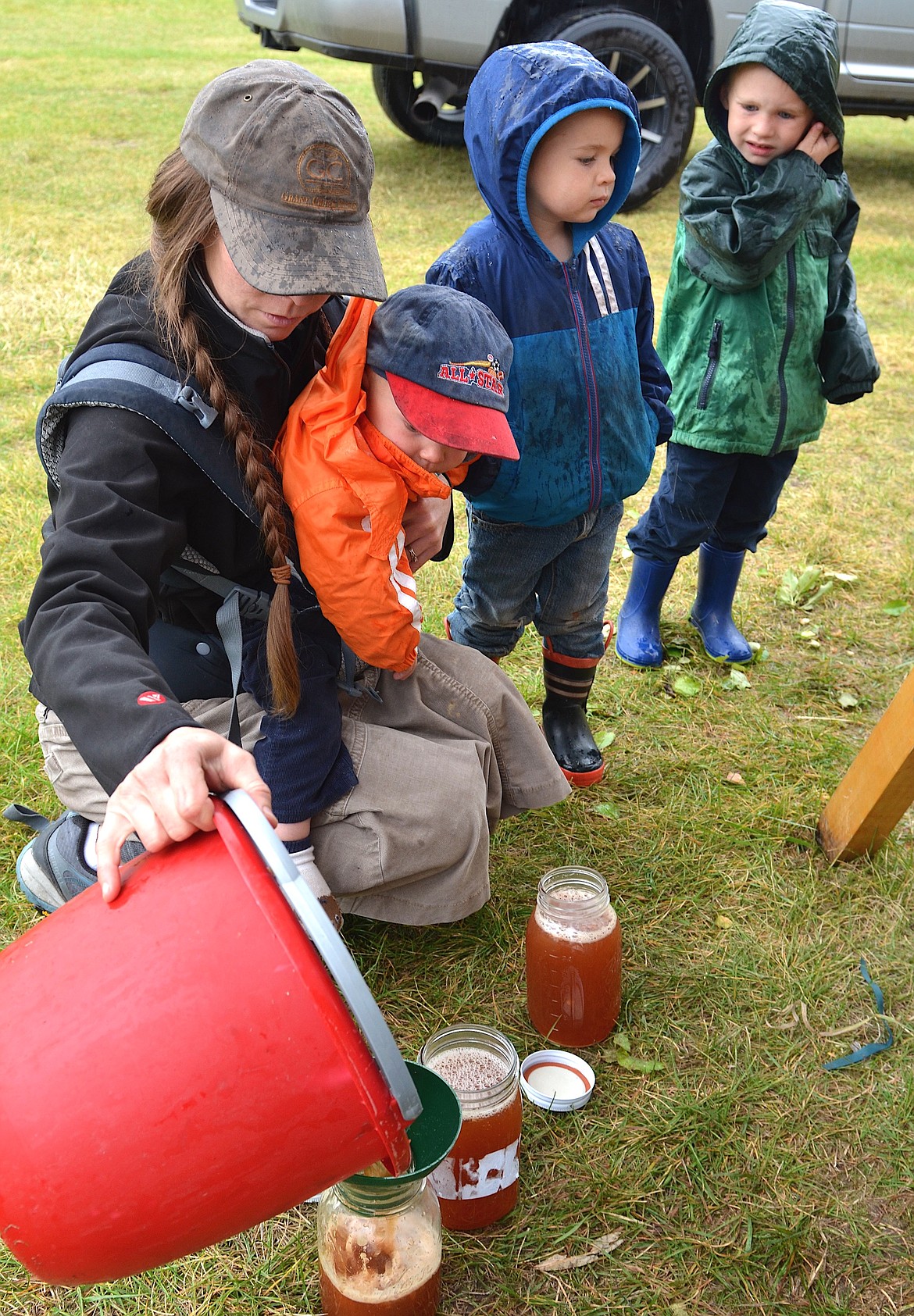 Lisa Stellmach pours fresh cider into jars as her three sons, Jeremiah, Isaiah and Elijah keep an eye on the process, and try to stay out of the rain. Three cider presses were available at the Fall Wildlife Festival in Ronan Saturday. (Kristi Niemeyer/Leader)