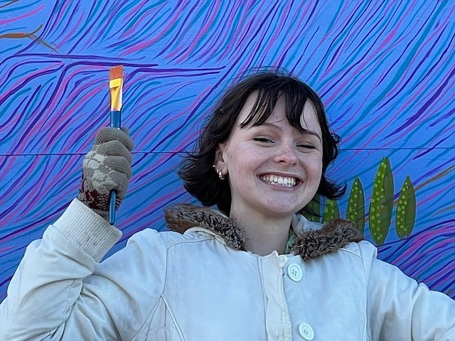 Local artist Emma Buchanan stands in front of the mural she painted in downtown Soap Lake, commissioned by the Soap Lake Creative District Planning Committee and the Friends of the Lower Grand Coulee.