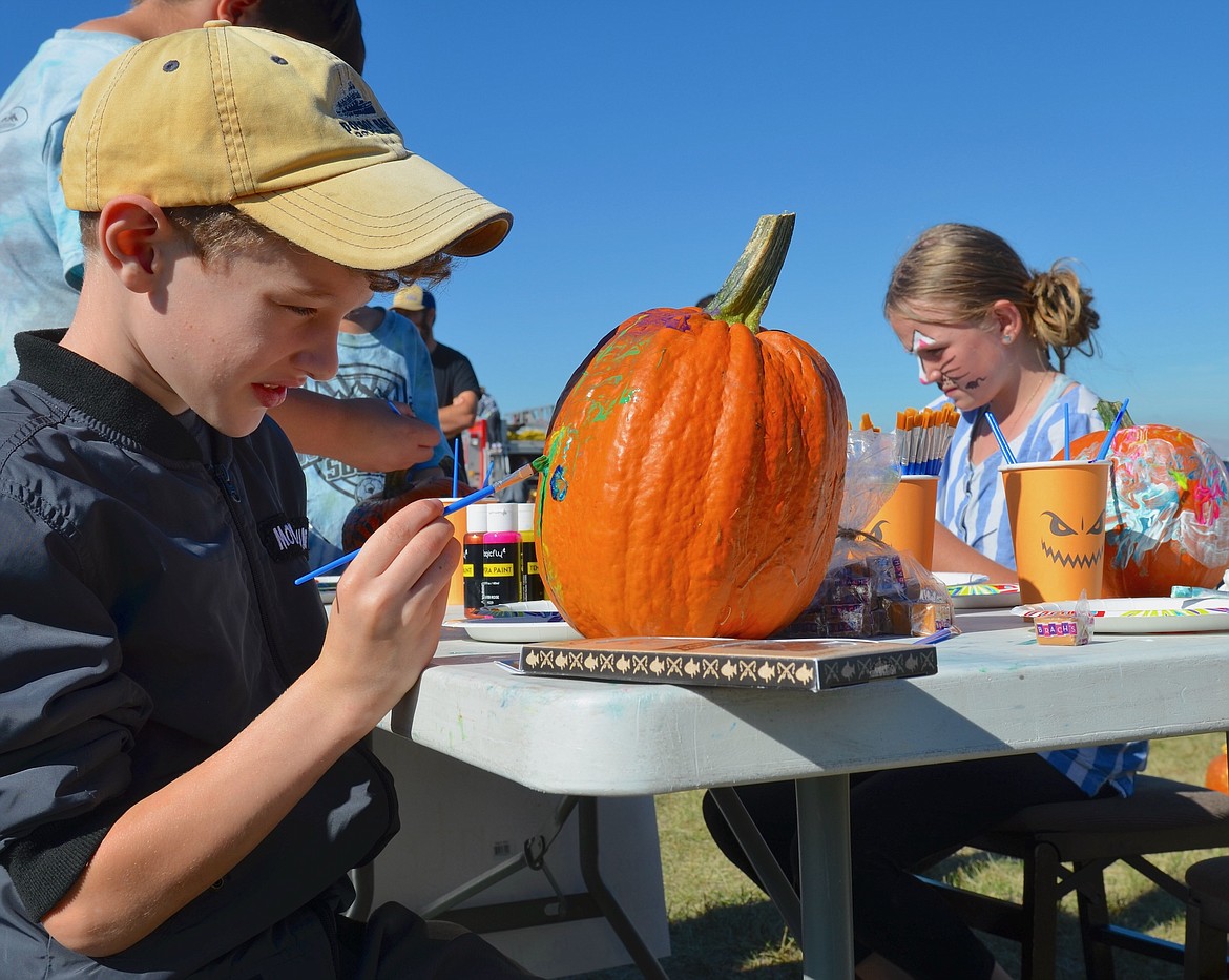 Pumpkin painters Silas Baird and Rebecca Higley wield brushes during Pumpkin Drop festivities at the St. Ignatius Airport. More than 70 pumpkins were put to use during the fundraiser.