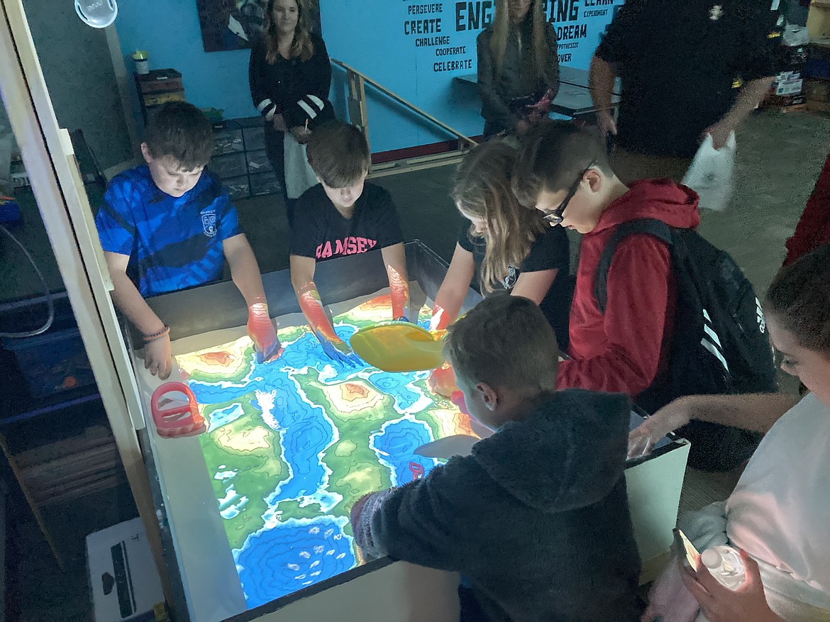 Students work together to create landforms in the augmented reality sandbox and experiment with how different topographies change the direction of water.