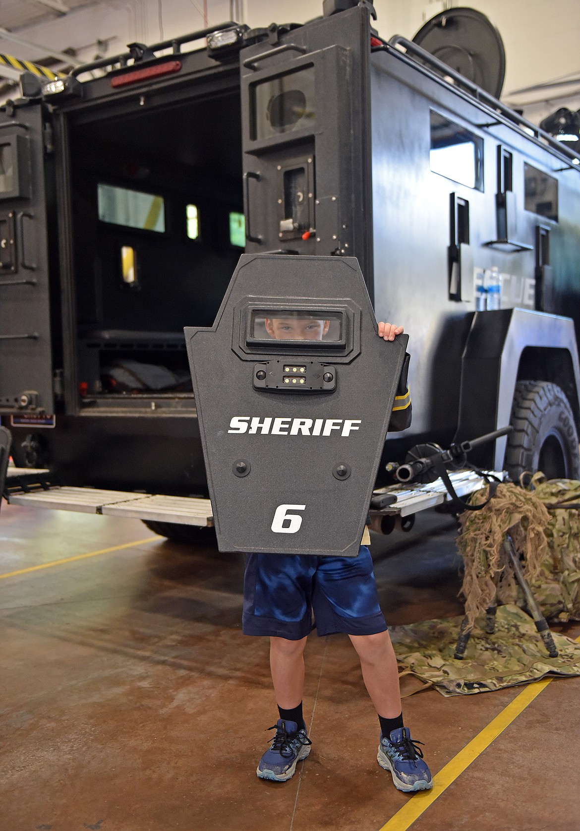 Seven-year-old Zevric Arseneaux peers out from behind a shield at the Emergency Services Center's open house last Sunday. (Julie Engler/Whitefish Pilot)