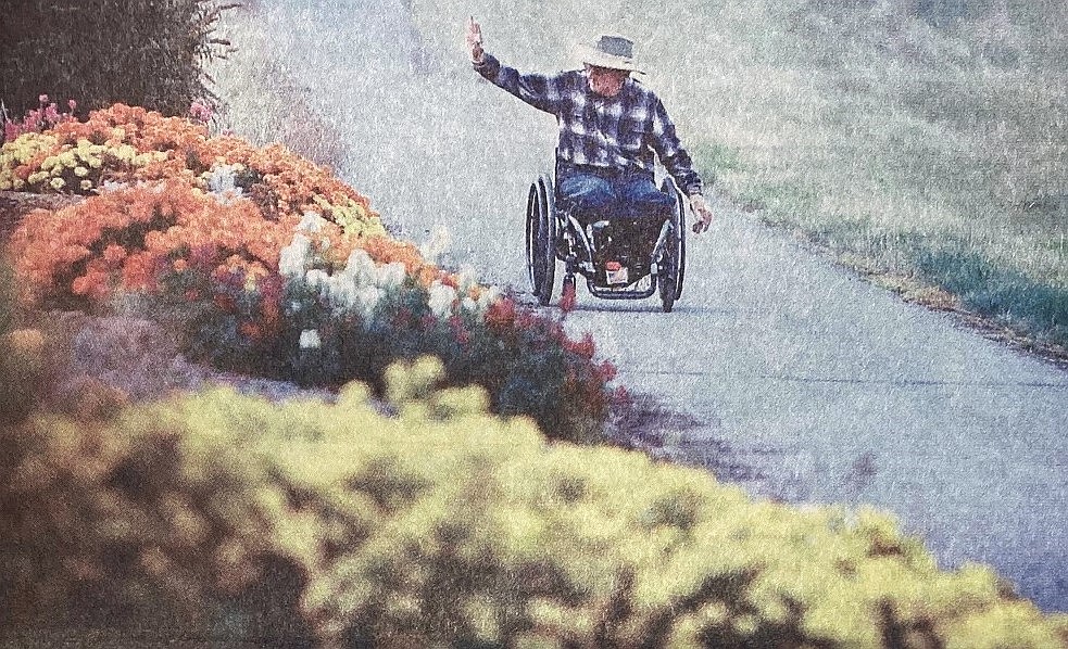 Indomitable Jerry Elston waves to a friend as he wheels along Highway 95 bike trail.