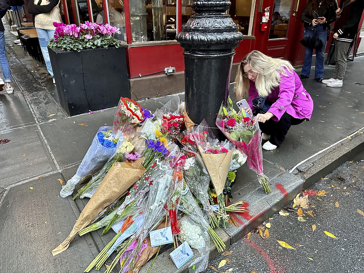 A person takes pictures of a makeshift memorial for Matthew Perry outside the building known as the "Friends" building in New York, Sunday, Oct. 29, 2023. Fans lingered in the rain, taking pictures and leaving flowers on the corner outside the building shown in exterior shots on the popular TV show. Perry, who played Chandler Bing on NBC’s “Friends” for 10 seasons, was found dead at his Los Angeles home on Saturday. He was 54. (AP Photo/Brooke Lansdale)