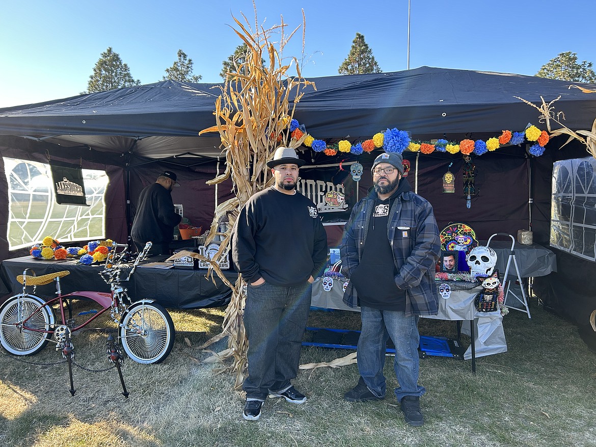 Lakesiders president Anthony Reyes and member Giovanni Maldonado stand in front of their tent at the front of the Trunk or treat. Next to them is the custom bike that they sold on auction.