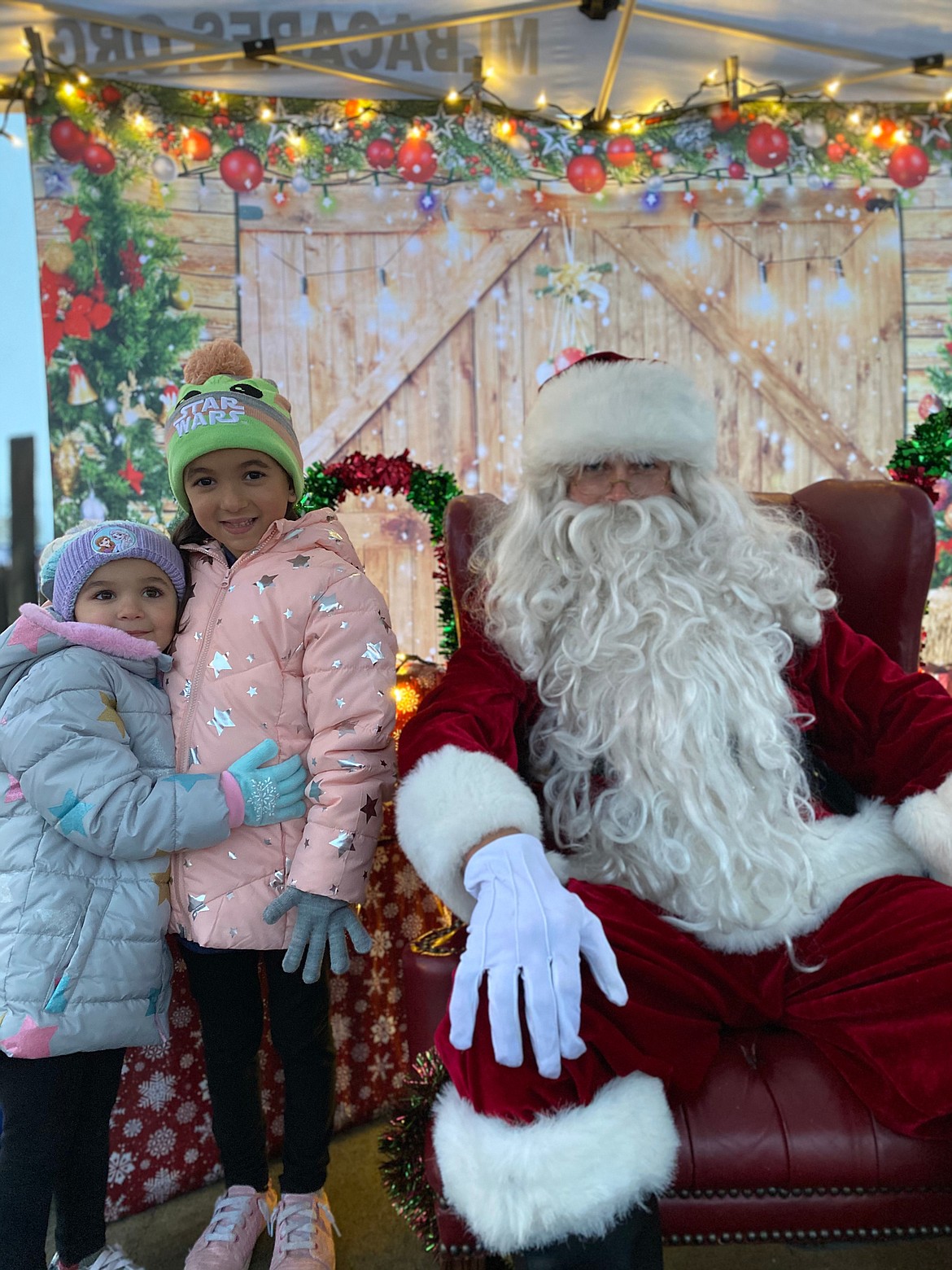 One of the 2022 Moses Lake Tree Lighting Santas sits next to two children in Sinkiuse Square. This year’s event will also feature someone dressed as Santa.