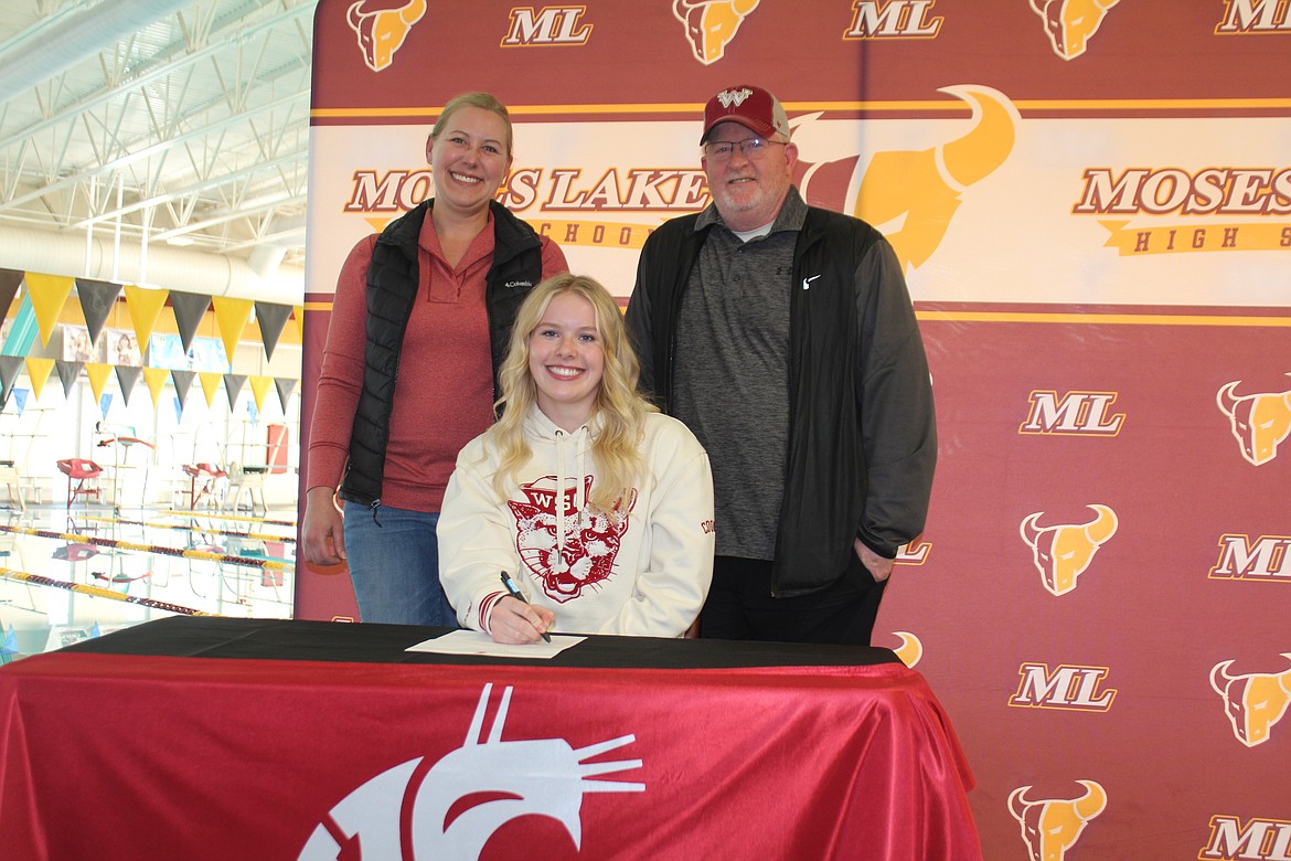Issabelle Parish, seated, signs a letter of intent to swim for Washington State University Wednesday afternoon in the company of her mom Cody Parrish, left, and dad Wade Parrish, right.