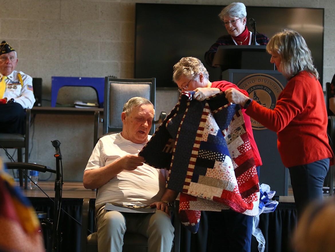 Vietnam War veteran Tom Young inspects his new Quilt of Valor during a ceremony Friday at the Idaho State Veterans Home in Post Falls. North Idaho Quilts of Valor coordinator Giannine O’Connor is holding up the blanket as Kathy Whetstine, right, assists.