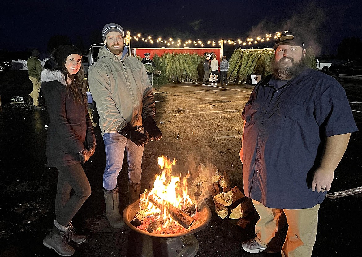 Aaron and Ala Griggs, left, and Rick Friesen warm themselves by the fire at All of Life Church's inaugural Giving Trees Christmas tree giveaway in 2022. The Post Falls church is hosting this year's event Saturday, where it will give away 300 Douglas fir trees to under-resourced families.