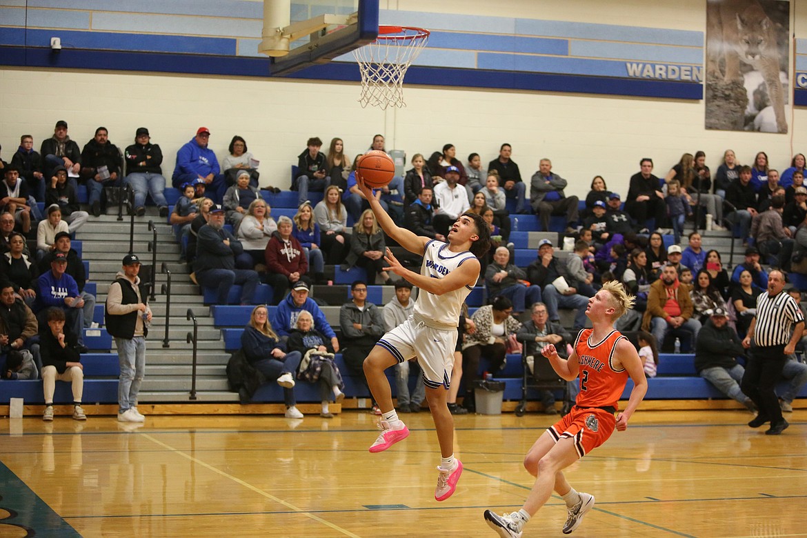 Warden junior Anthony Gutierrez, in white, rises toward the rim while attempting a lay-up.