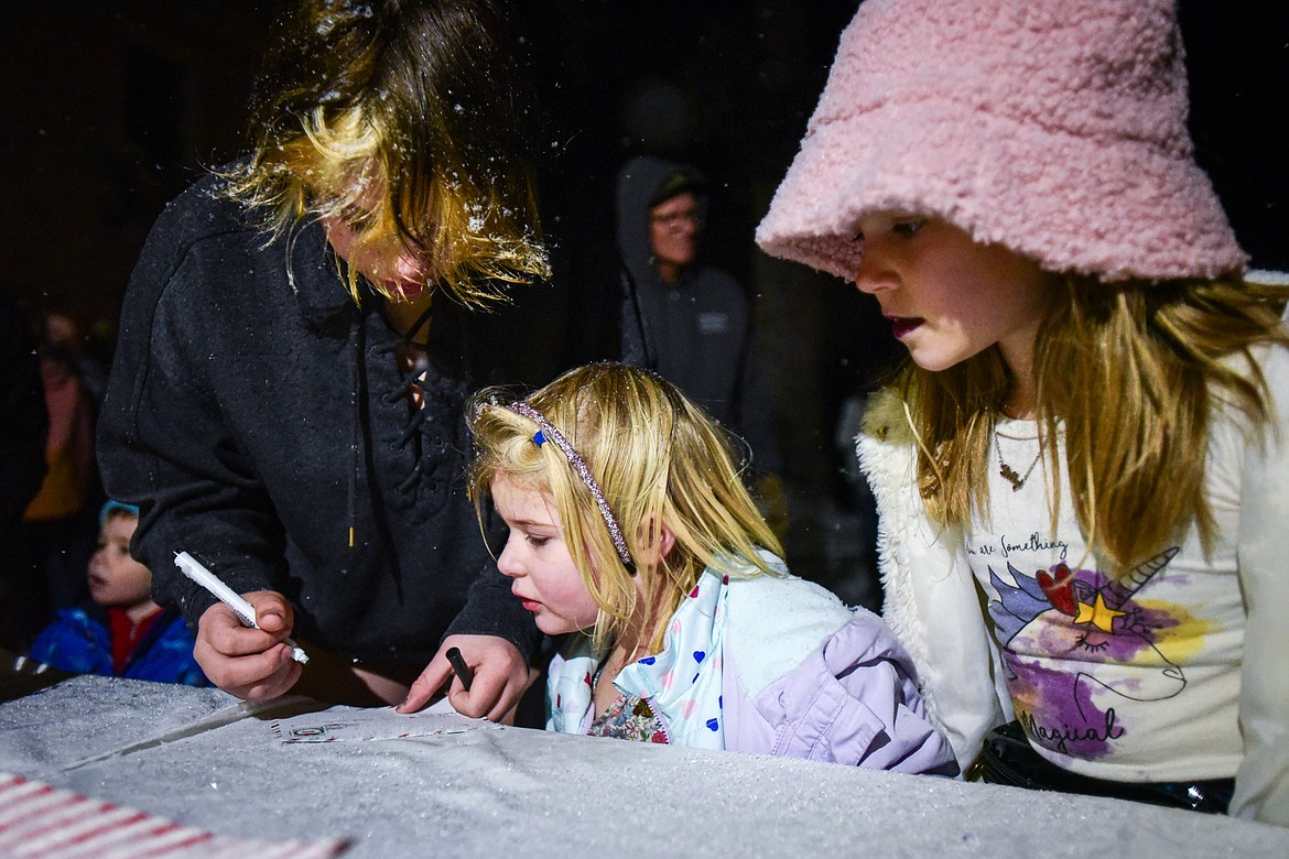 From left, Madison Baier, Addy Baier and Lilly Moen write a letter to Santa Claus outside Johnson Funeral Home during the Downtown Kalispell Holiday Stroll and Tree Lighting on Friday, Dec. 1. (Casey Kreider/Daily Inter Lake)