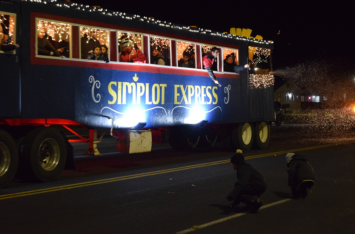 The Simplot Express parade float coasts west on Main Street during Othello’s Christmas celebration Saturday while kids rush to pick up candy and the float blows fake snow out onto the street.