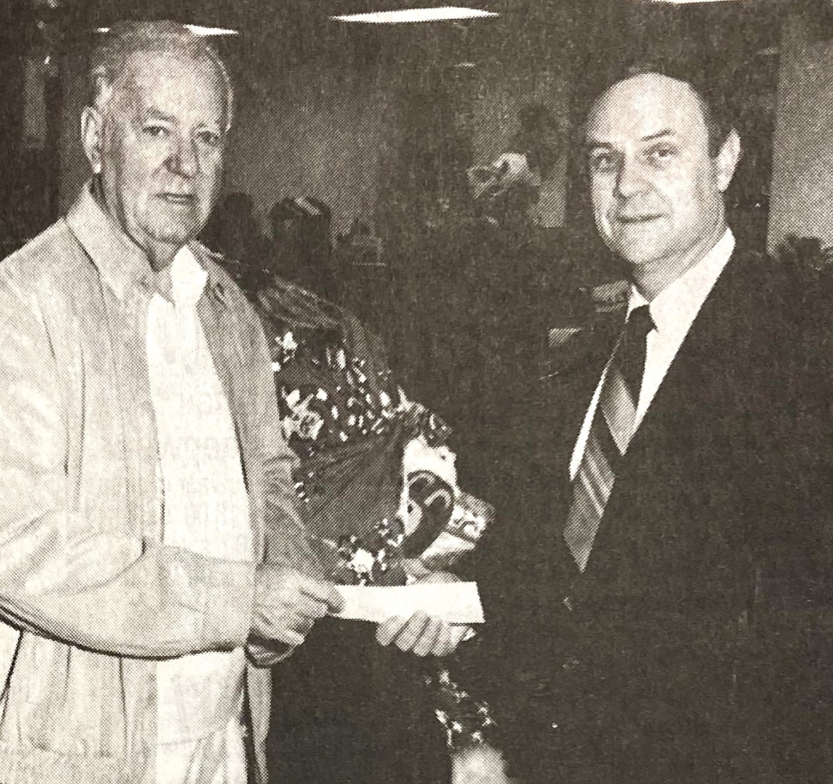 When he wasn't writing columns for the Coeur d'Alene, Bob Paulos, left, was drive chairman for the paper's Christmas for All program. Here, he's shown accepting a check from Parker Woodall of Northern State Bank.