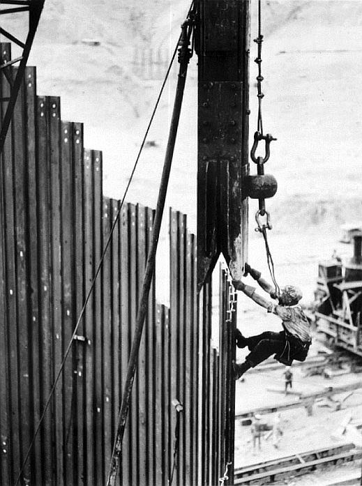 A worker sets a steam hammer to pound in piles for a temporary dam, called a cofferdam, at the site of Grand Coulee in August 1936.