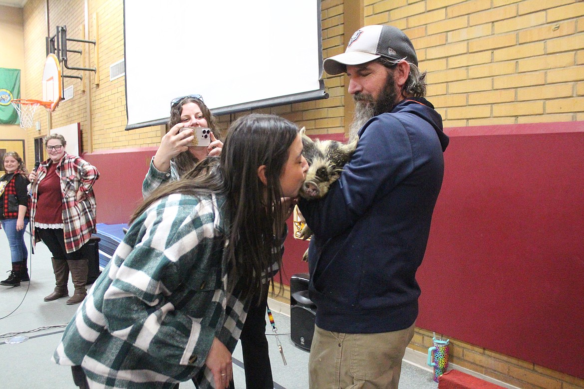 Keiley Warkentin, kindergarten teacher at Midway Elementary School, kisses a cute little pig during Friday’s monthly school assembly. Jonathan Underwood holds the pig.