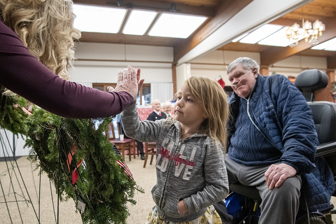 Montana Veterans Home coordinator Denise Holm gives Annie Carver a high-five after helping veteran James Hux hang his wreath during Wreaths Across America event on Saturday, Dec. 16. (Avery Howe photo)