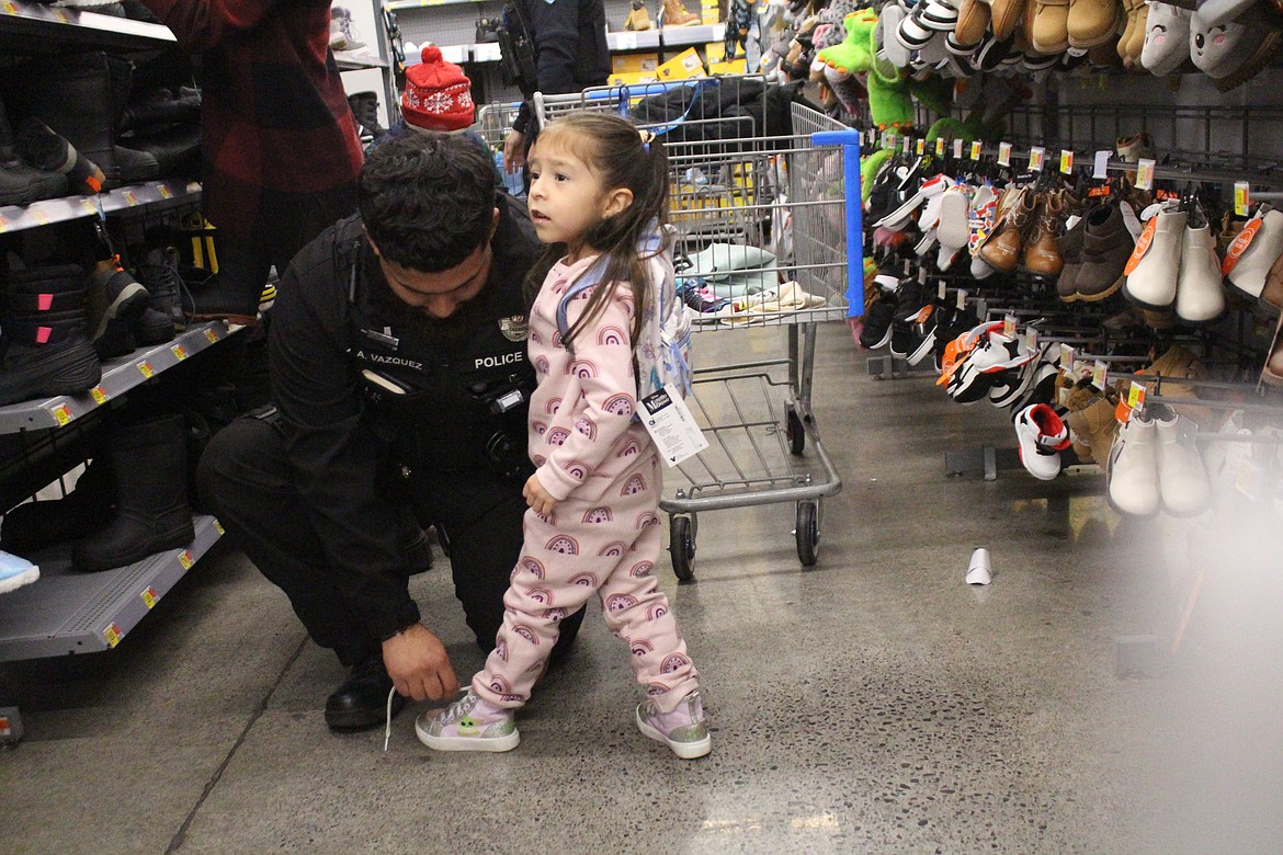 Moses Lake Police Department Officer Alejandro Vazquez, left, stops to tie a shoe for Kamilla, one of his shopping buddies.